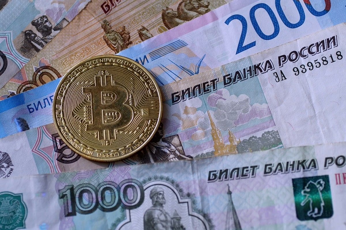 A metal token intended to represent Bitcoin rests on a collection of Russian banknotes.